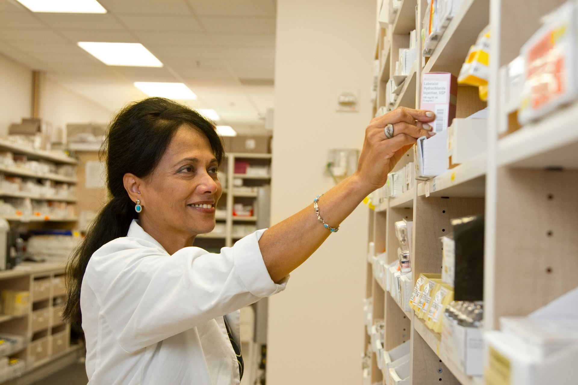 Picture of a pharmacist reaching for some medicine on a shelf